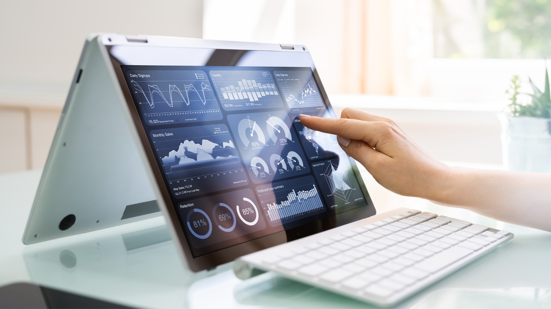 A woman's hand touching a laptop screen displaying various data reports